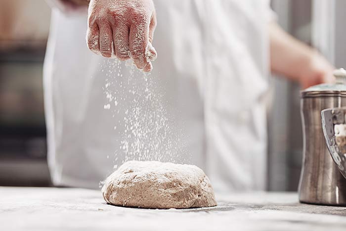 baker adds flour to sourdough on the table to bake the bread